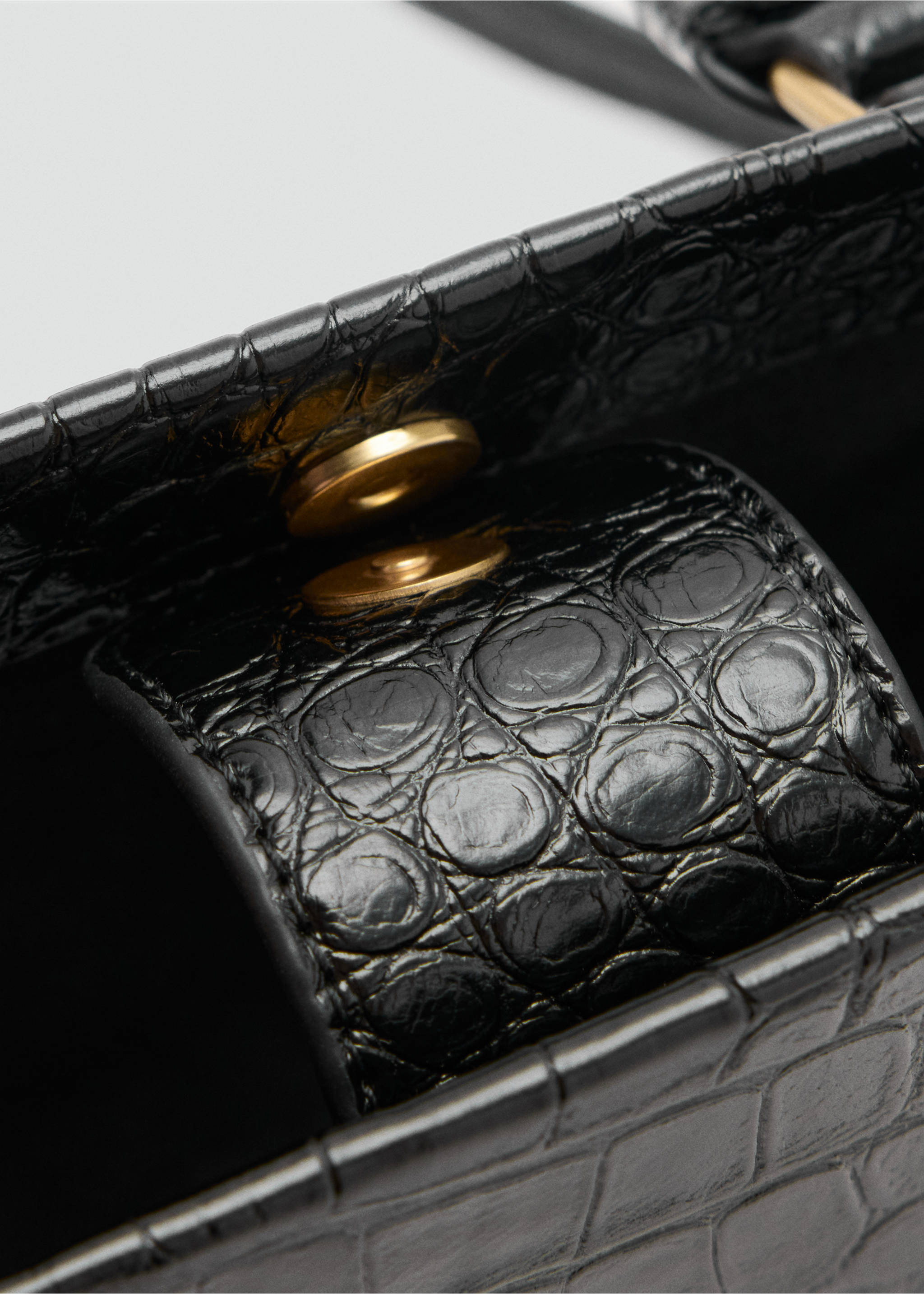 Close-up of a black crocodile-embossed cross-body bag with a gold-tone magnetic closure., Black. Ref: 47071340-00.