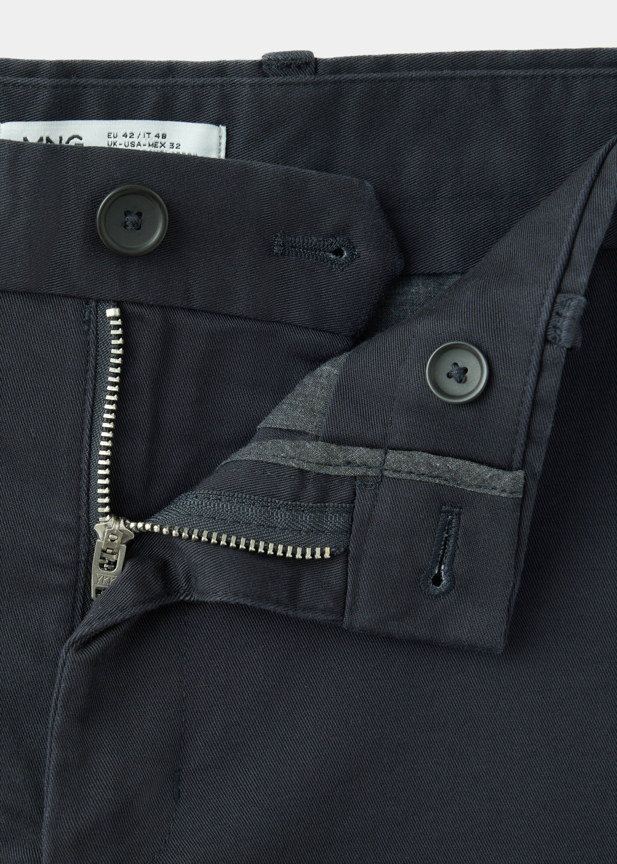 Close-up of the textured fabric and button fastening on dark grey trousers.