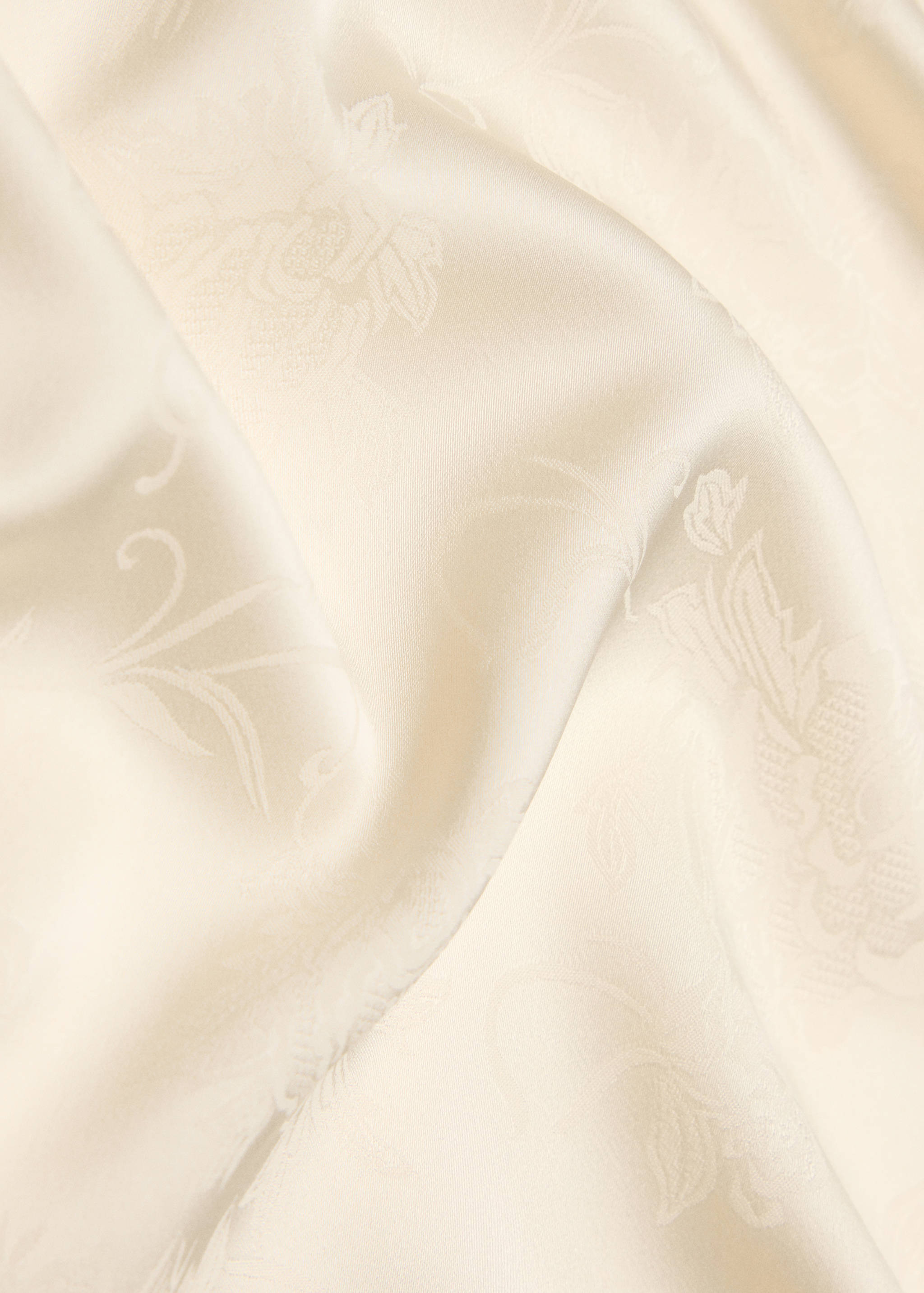 Close-up of a cream scarf with a tonal floral jacquard pattern.