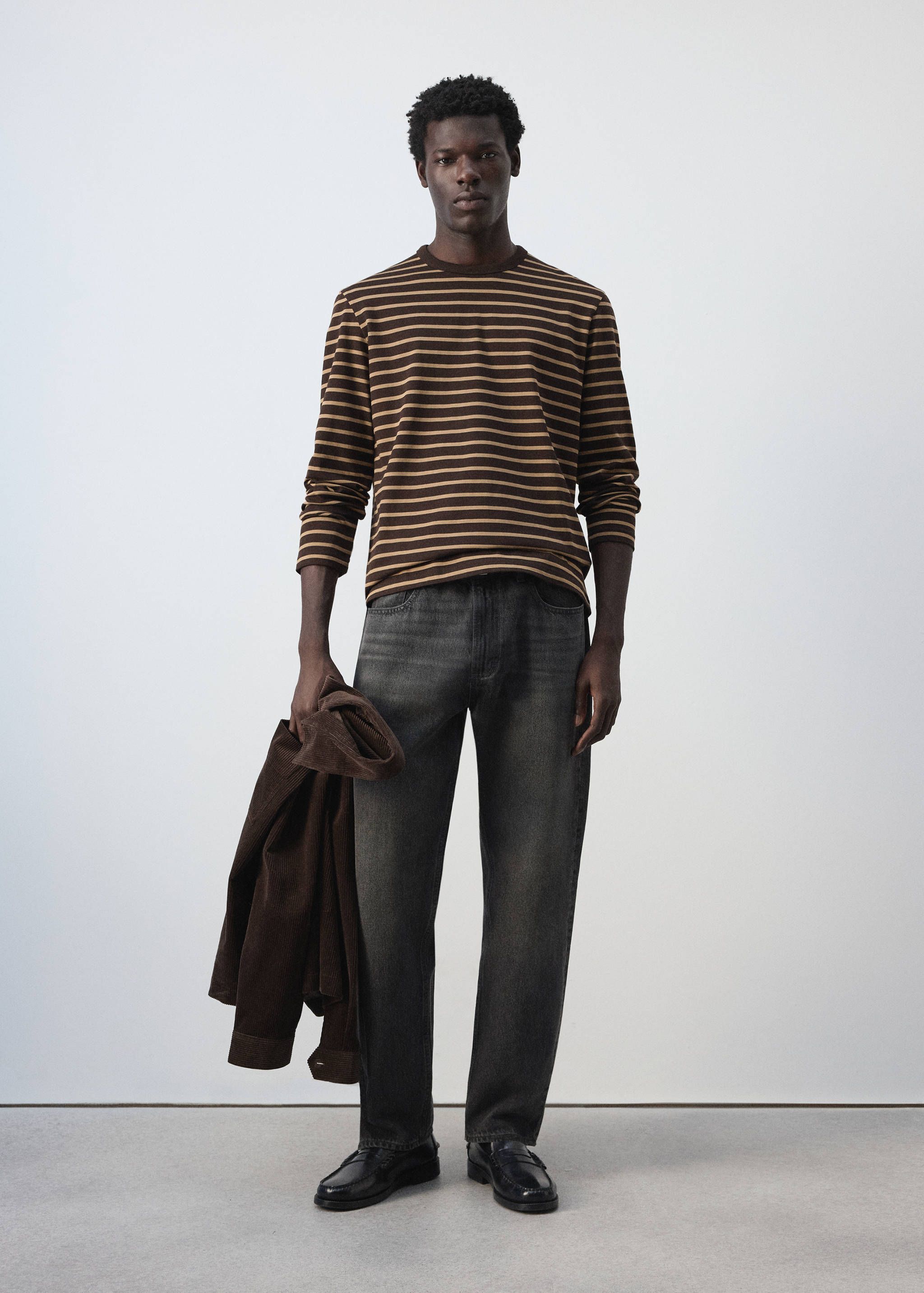 Brown and beige striped long-sleeve t-shirt with crew neck, worn with dark grey trousers.