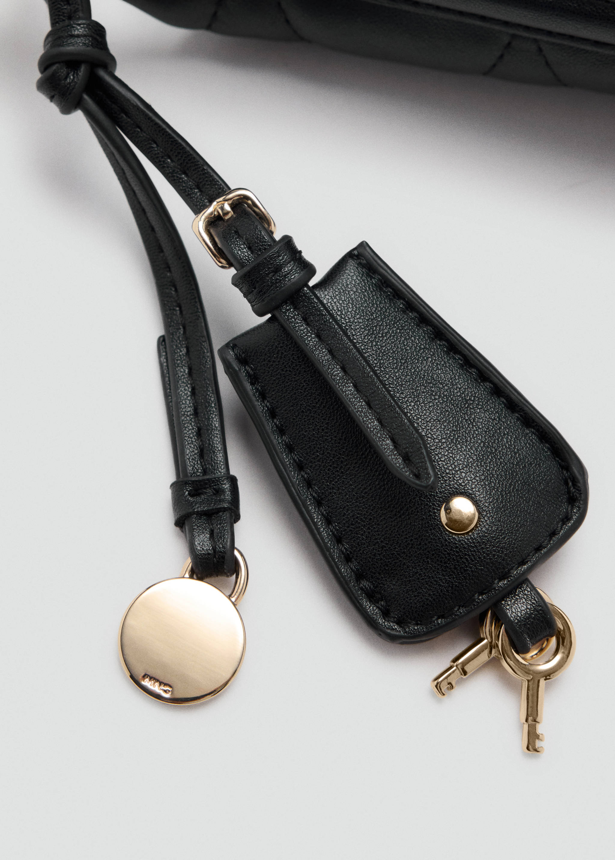 Primer plano del detalle de un bolso saco negro con un charm de piel, llaves doradas y herrajes metálicos.