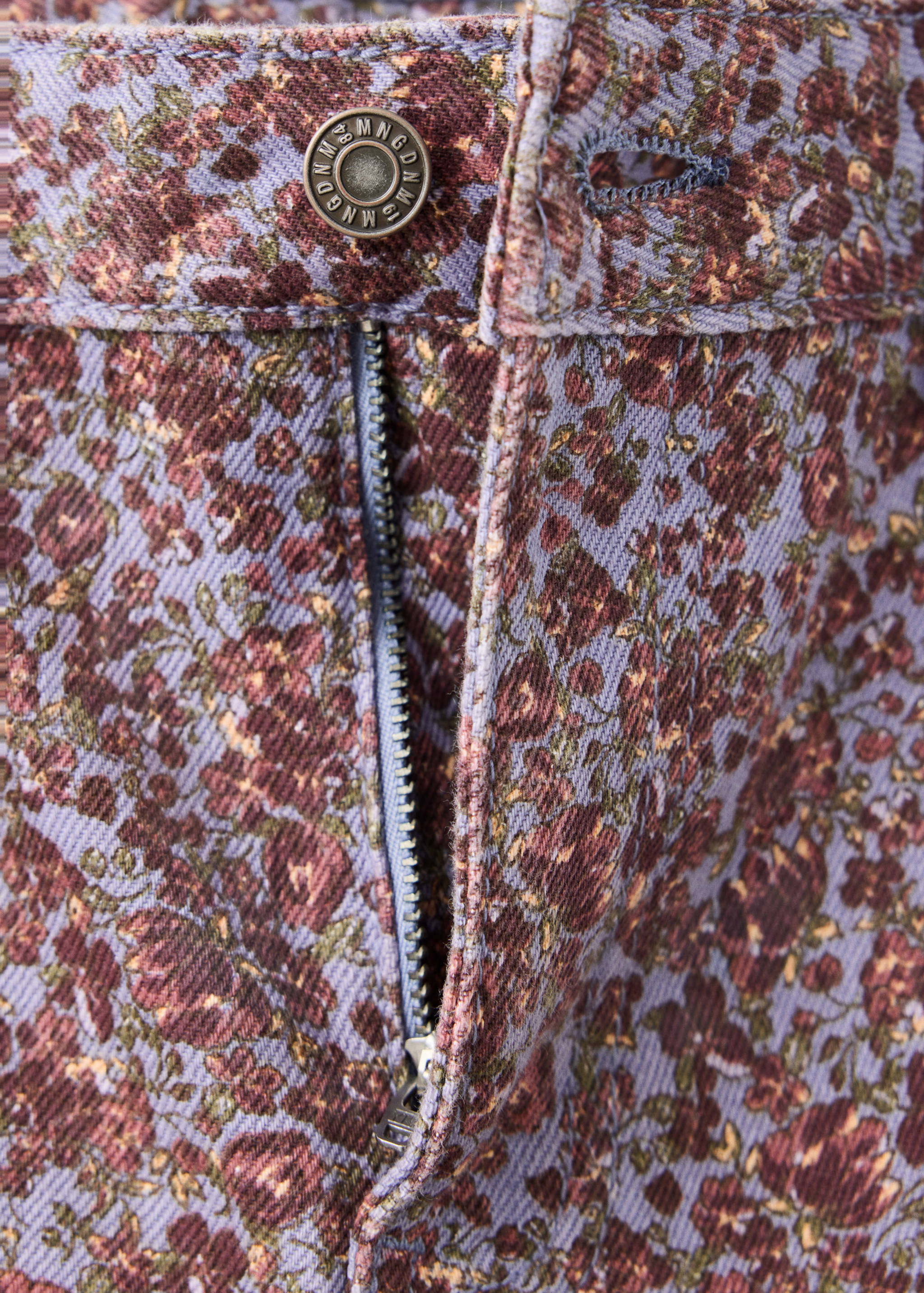 Close-up of the waistband and fly on purple floral print denim trousers.