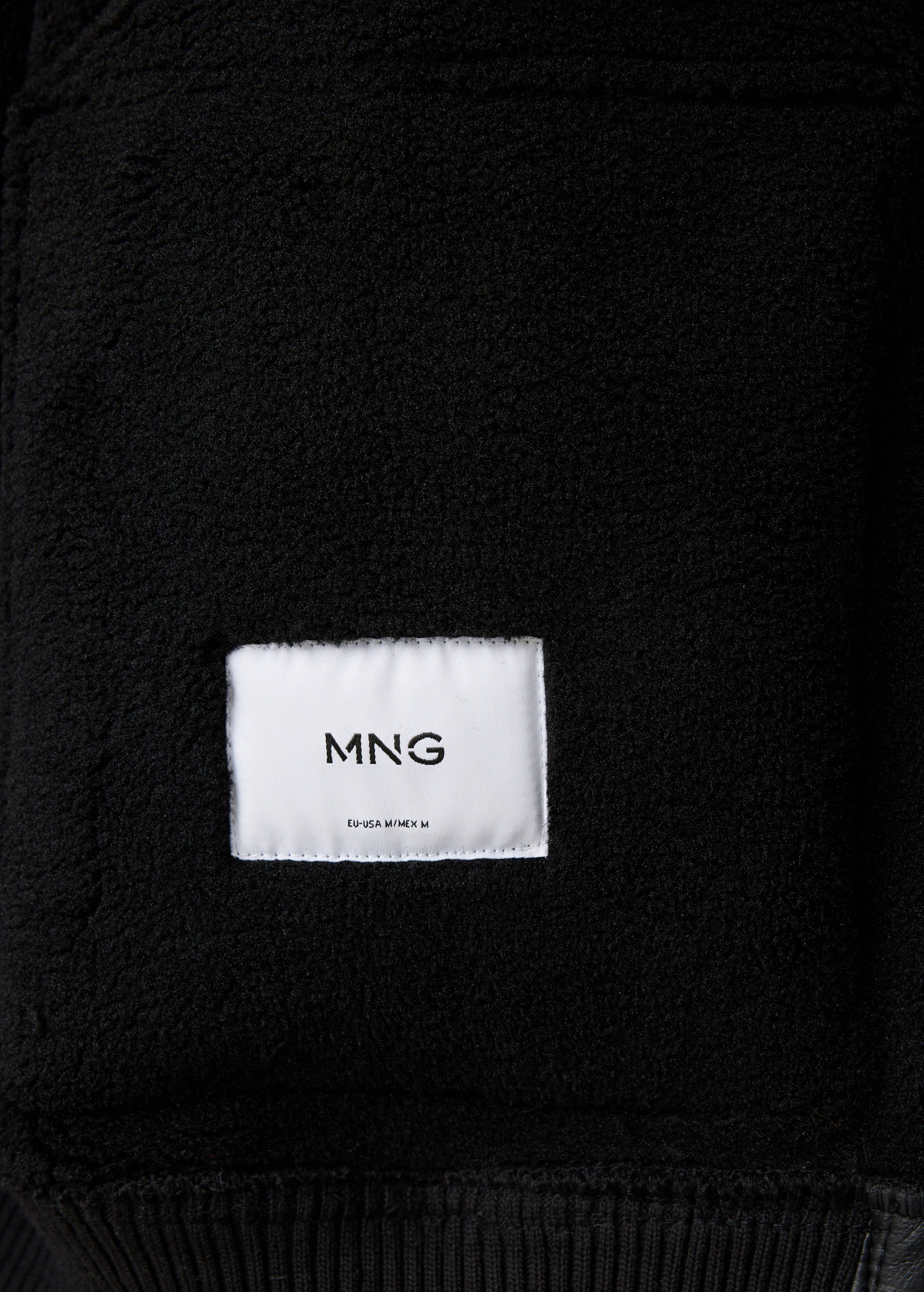 Close-up of black jacket interior with faux-shearling lining and MNG label.