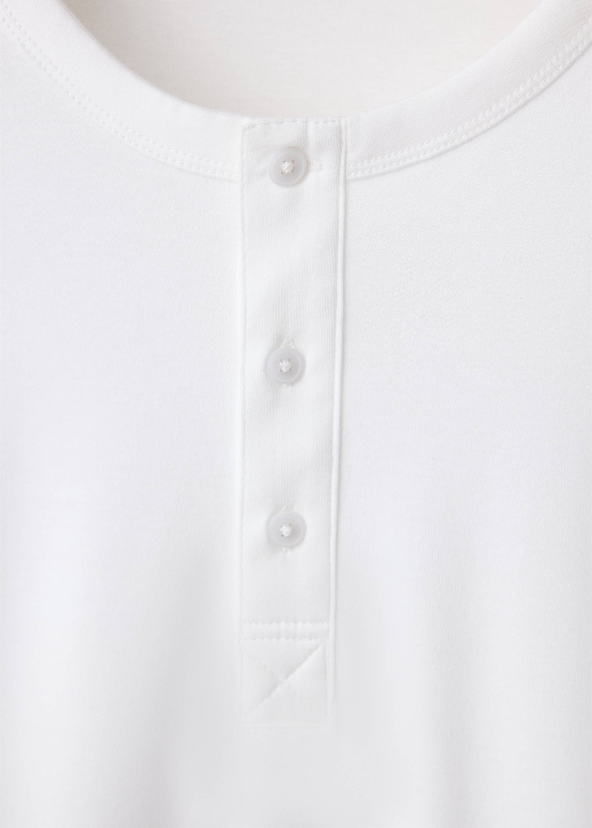 Detalle de camiseta blanca que muestra un cuello redondo y una tapeta de botones.