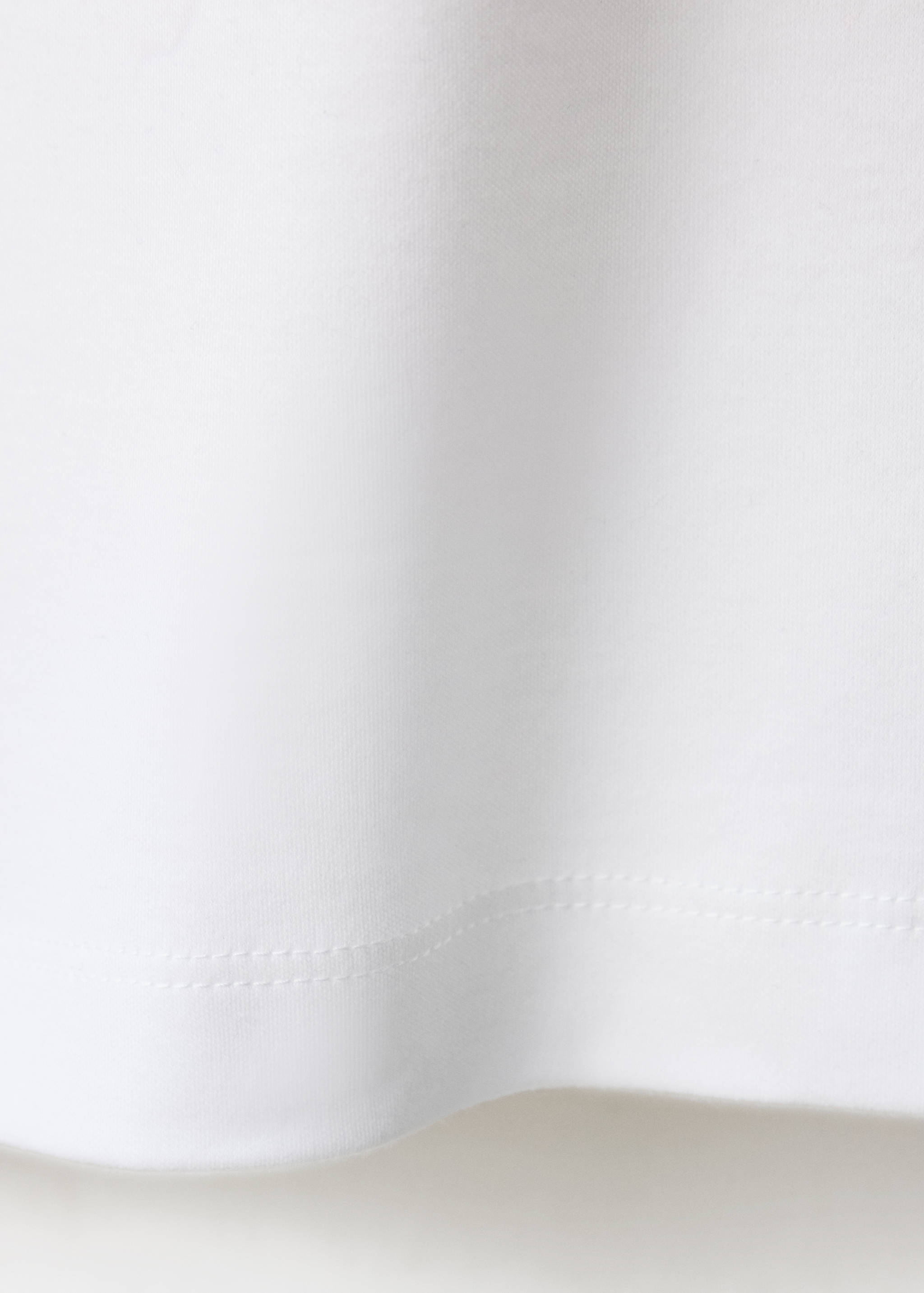 Primer plano de la textura del tejido y detalle del dobladillo de la camiseta blanca.