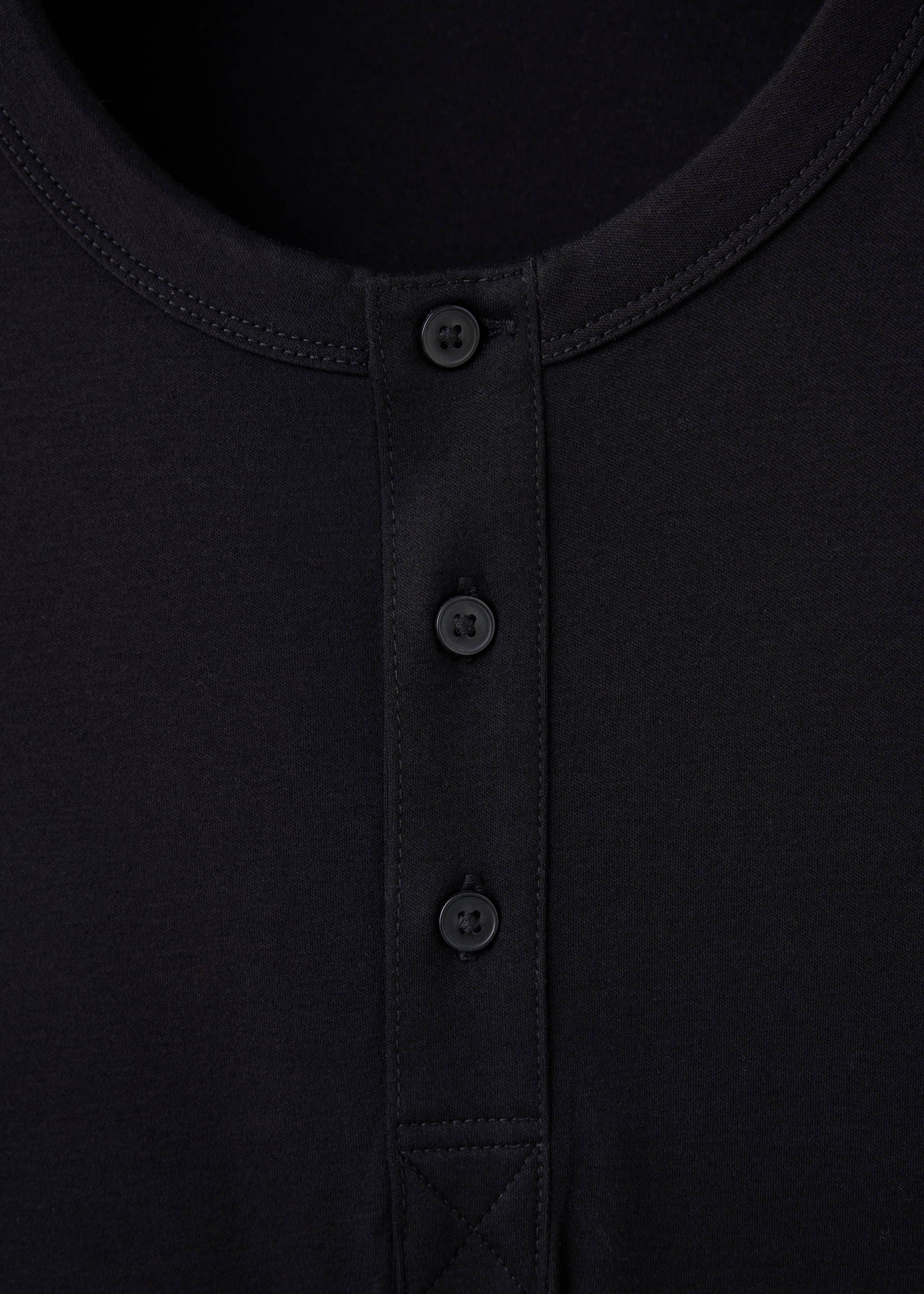 Detalle de camiseta negra que muestra el cuello redondo y la tapeta de botones.