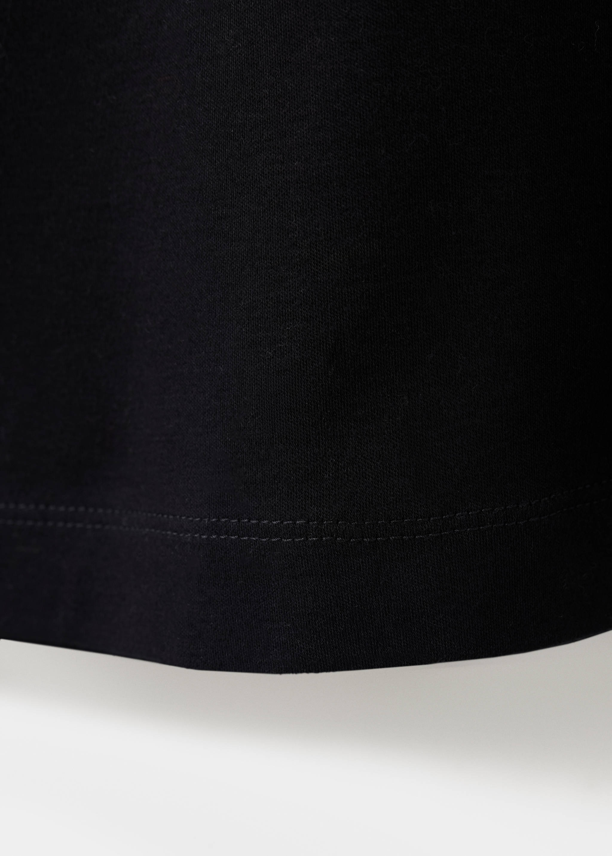 Detalle del tejido y del bajo de la camiseta negra en color negro.