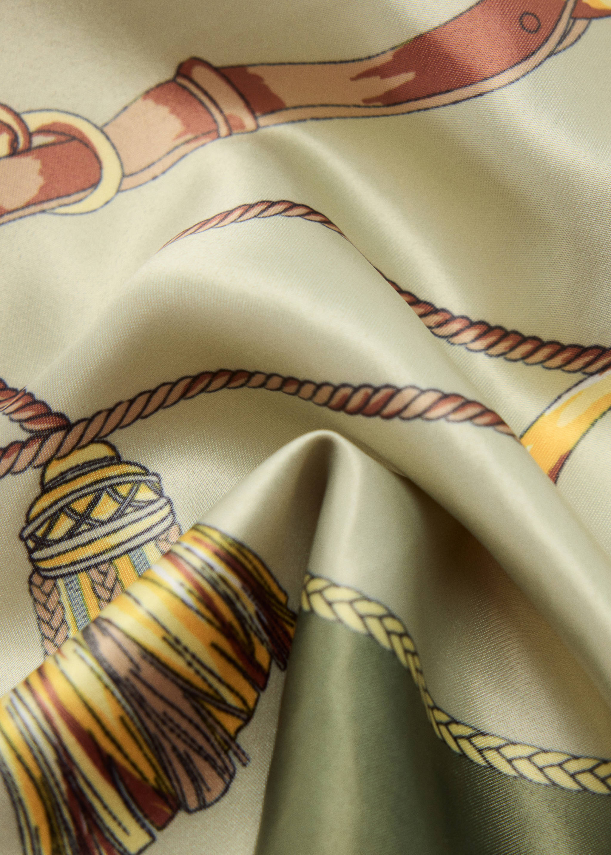 Close-up of a green silk scarf with a rope, belt, and tassel pattern.