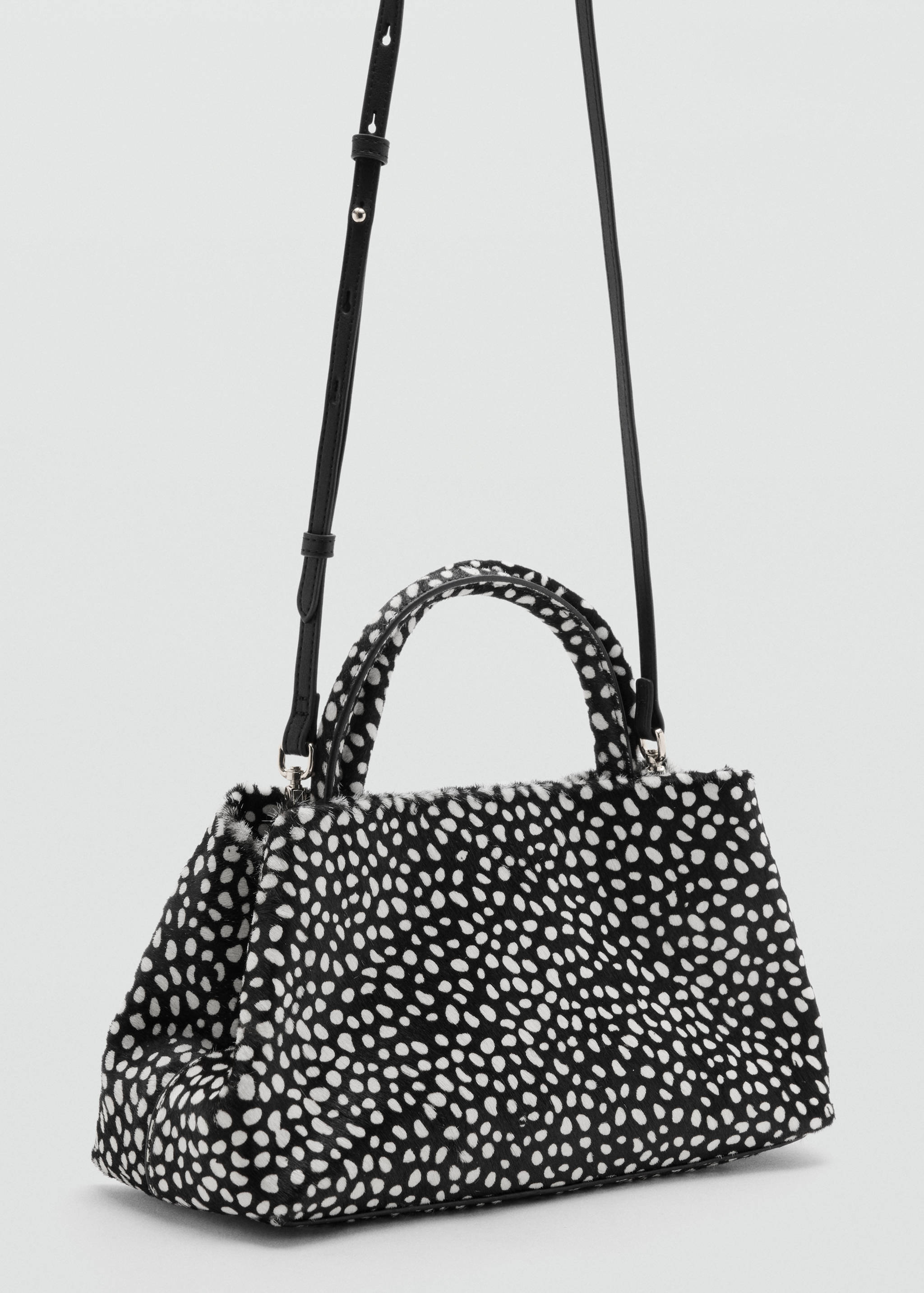 Black and white dalmatian-print faux-fur handbag with top handles and a black shoulder strap.