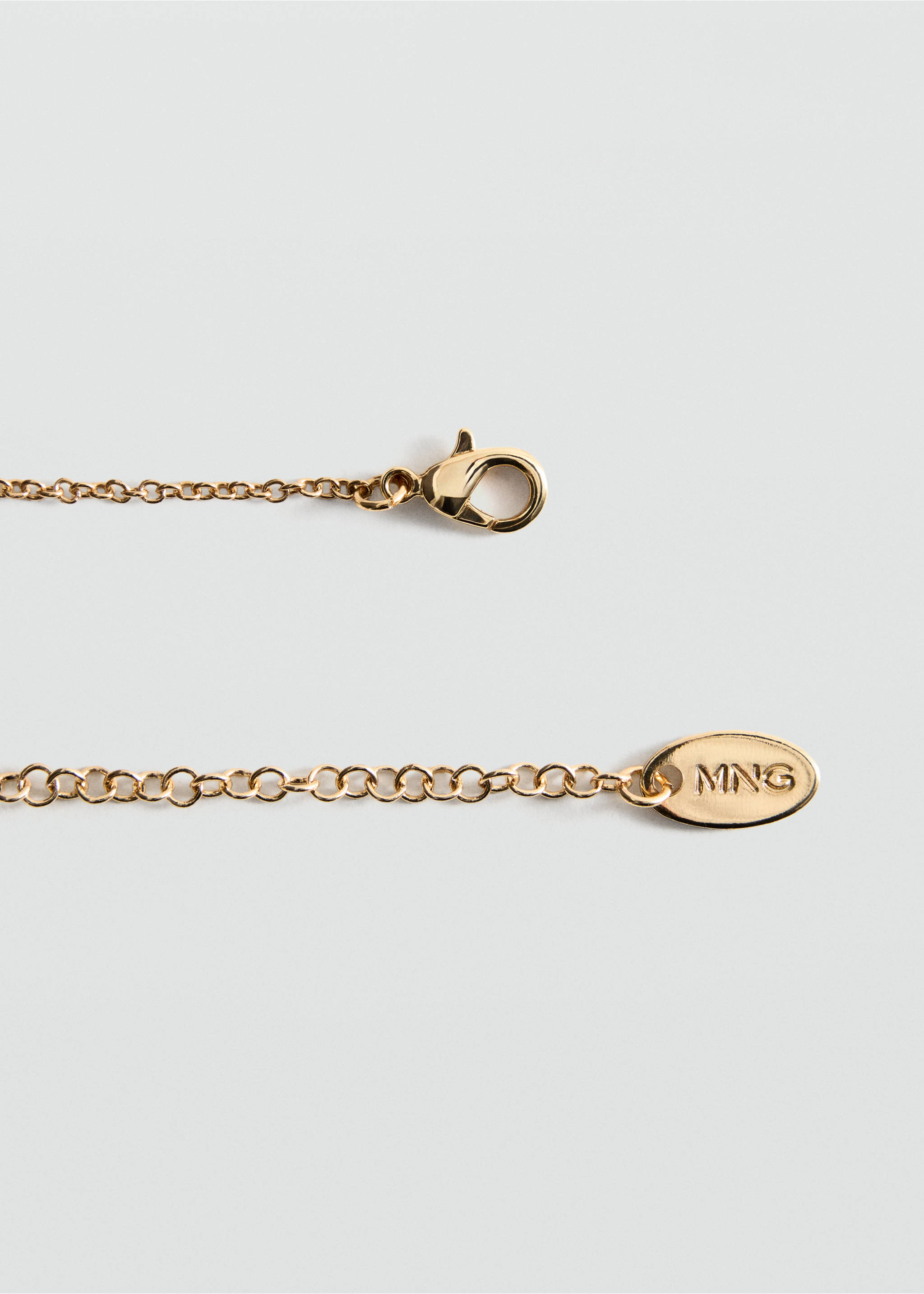 Primer plano de un collar gargantilla en tono dorado con cierre de mosquetón y abalorio con el logotipo de MNG., Oro. Ref: 47091385-00.