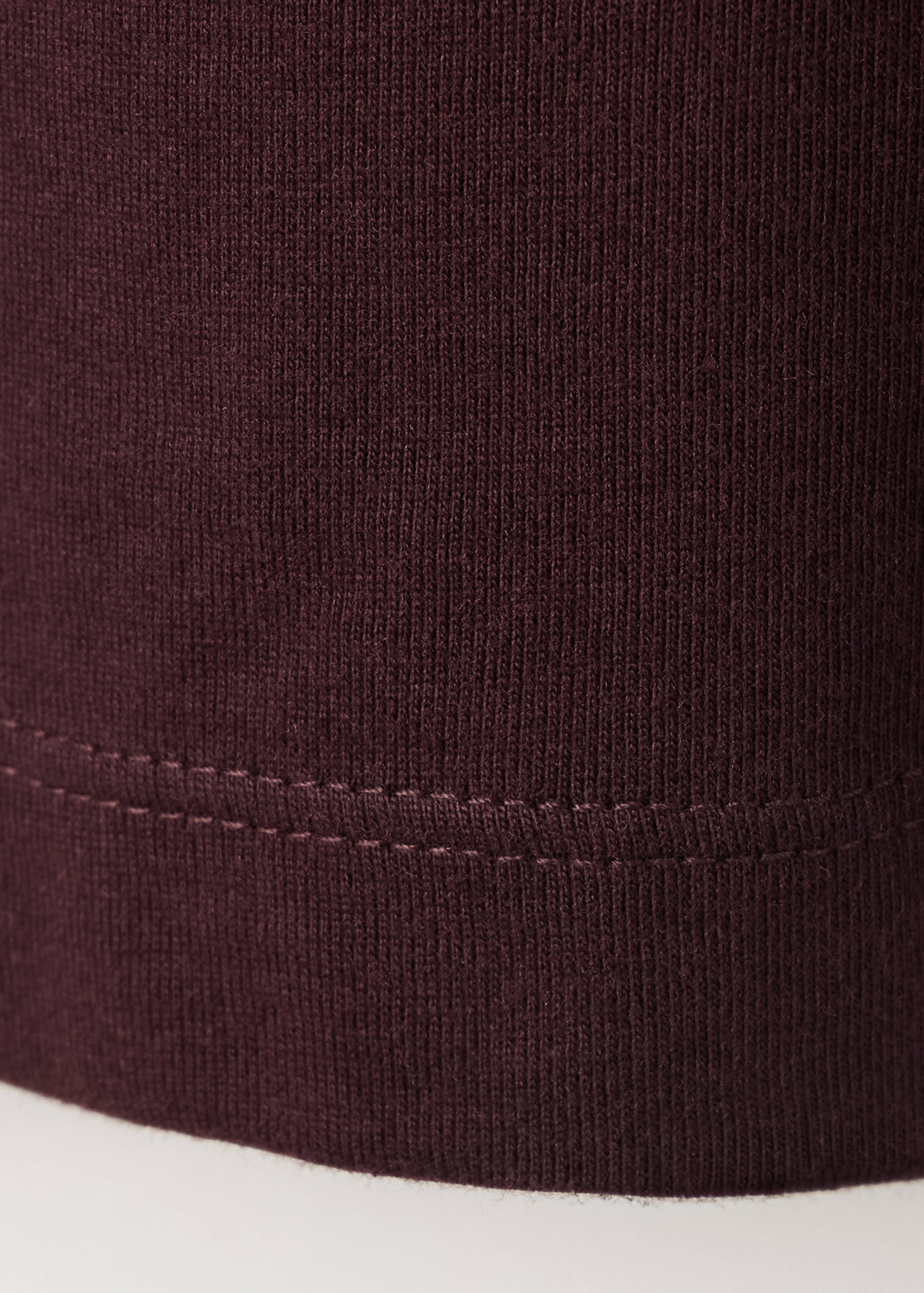 Close-up of the fine ribbed knit fabric and stitched hem on a dark burgundy t-shirt.