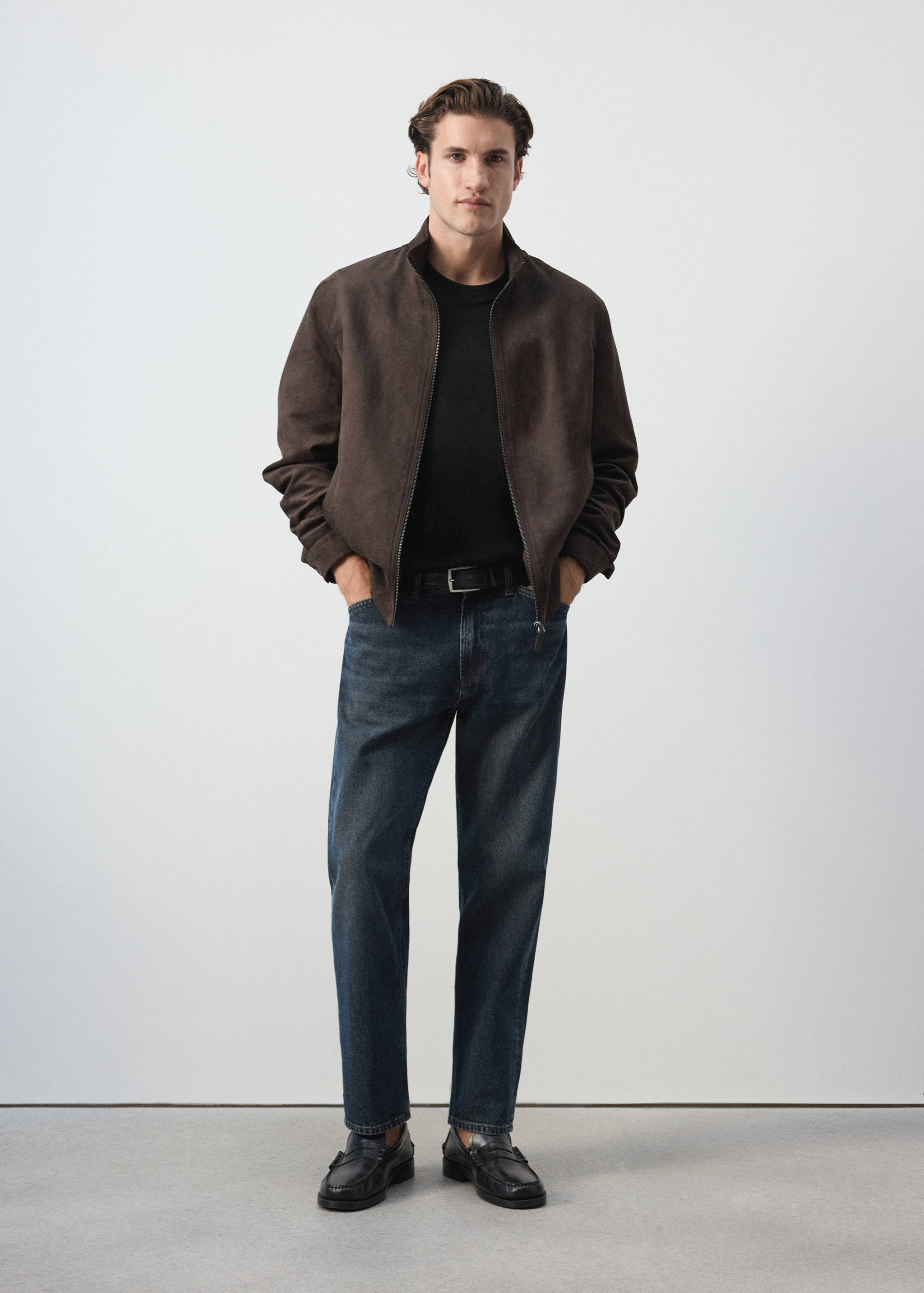 Black t-shirt worn with dark blue denim trousers and a brown jacket.