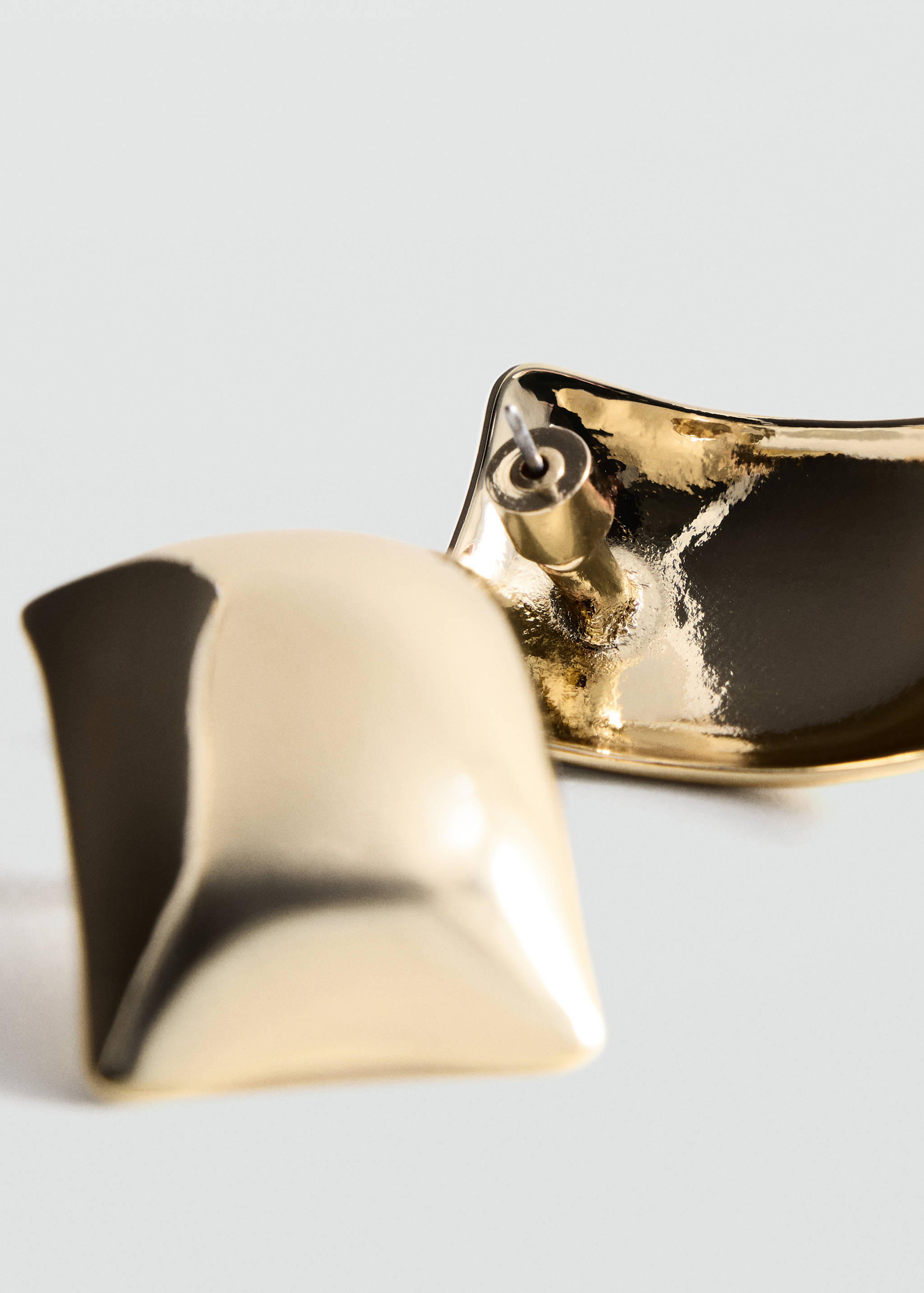 Glossy gold curved square earring in a three-quarters close-up.