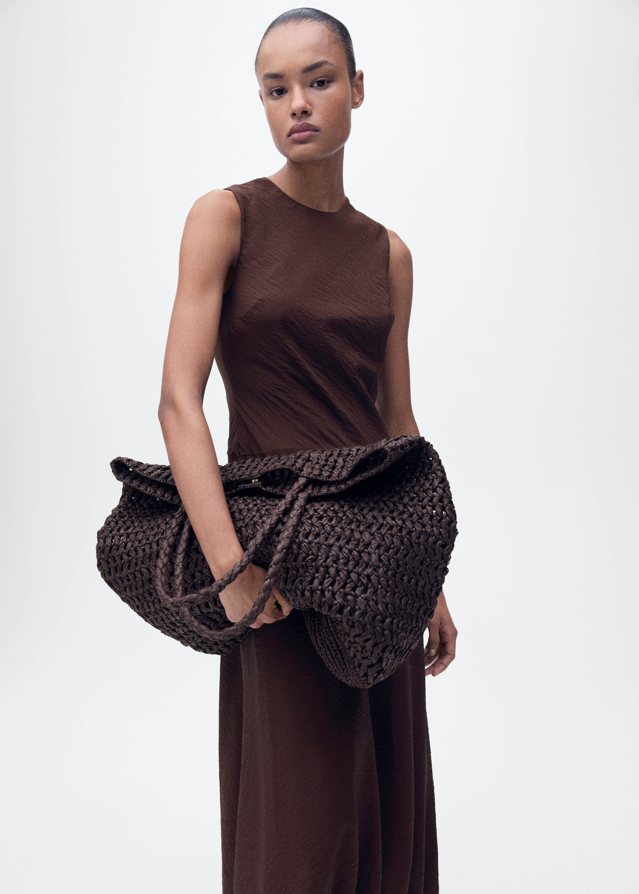 Large dark brown woven tote bag with braided handles, held by a model.