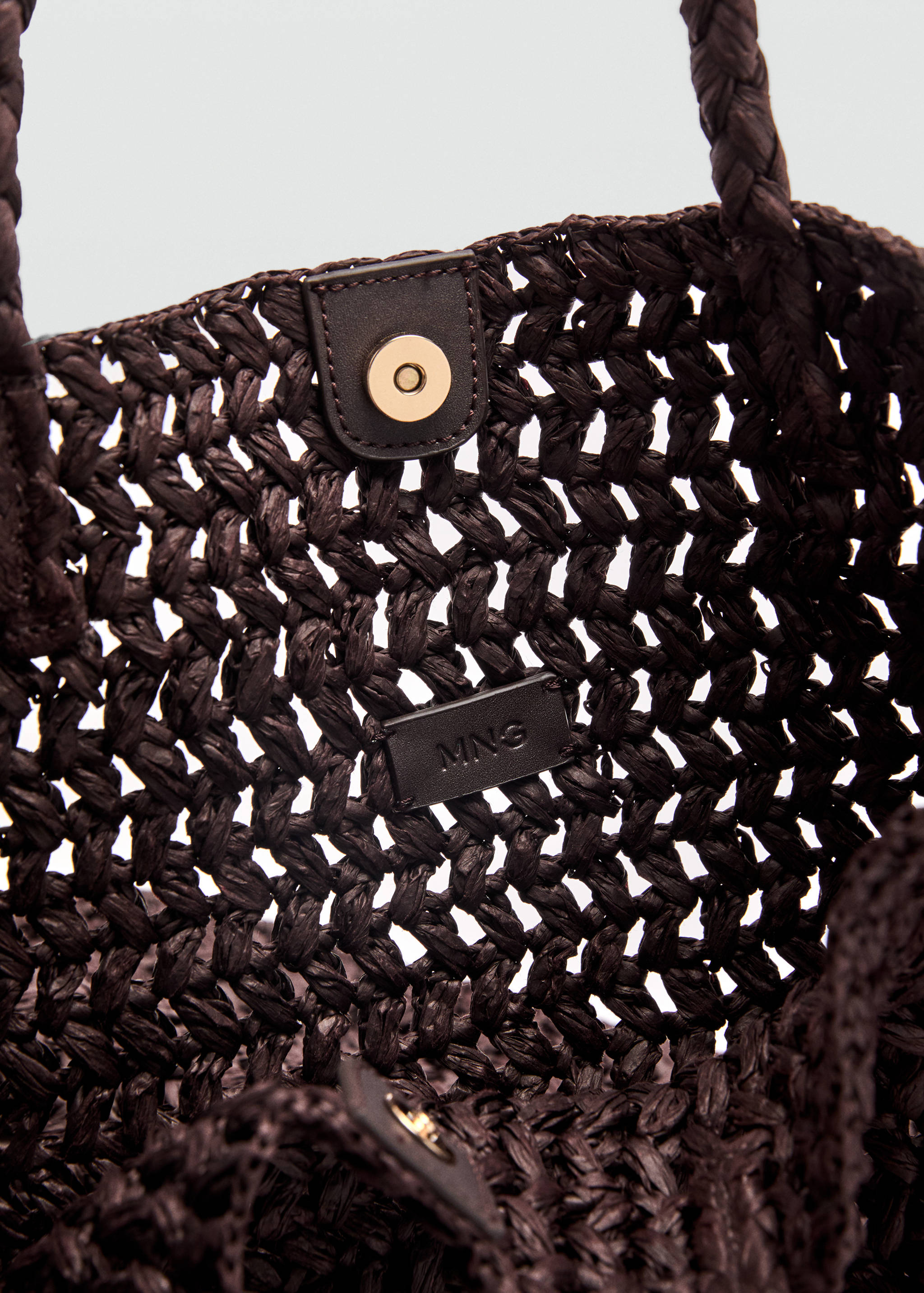 Close-up of the interior of a dark brown woven bag showing its snap closure and brand label.