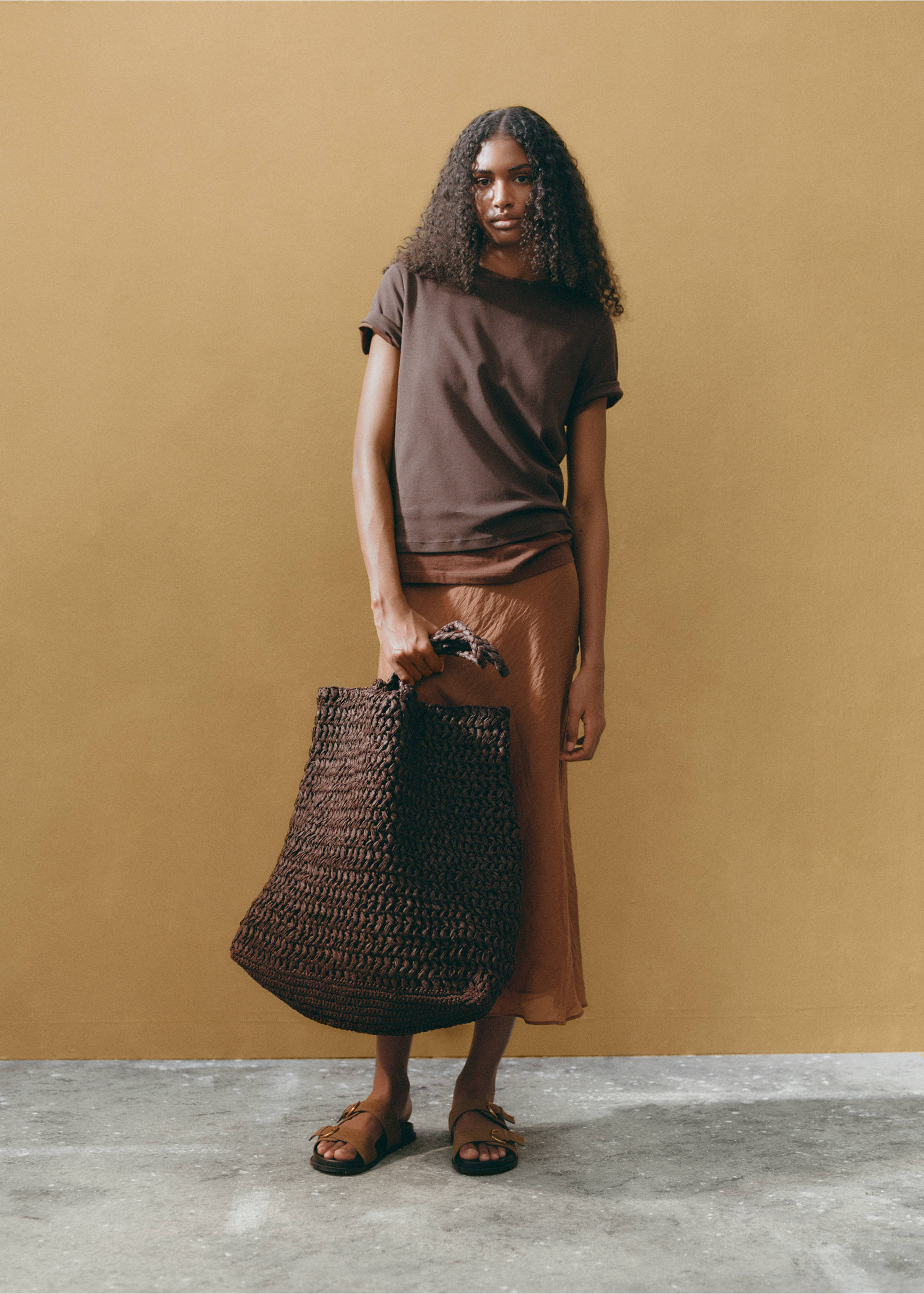 Dark brown woven tote bag held by a model wearing casual brown separates., Chocolate. Ref: 87007165-01.