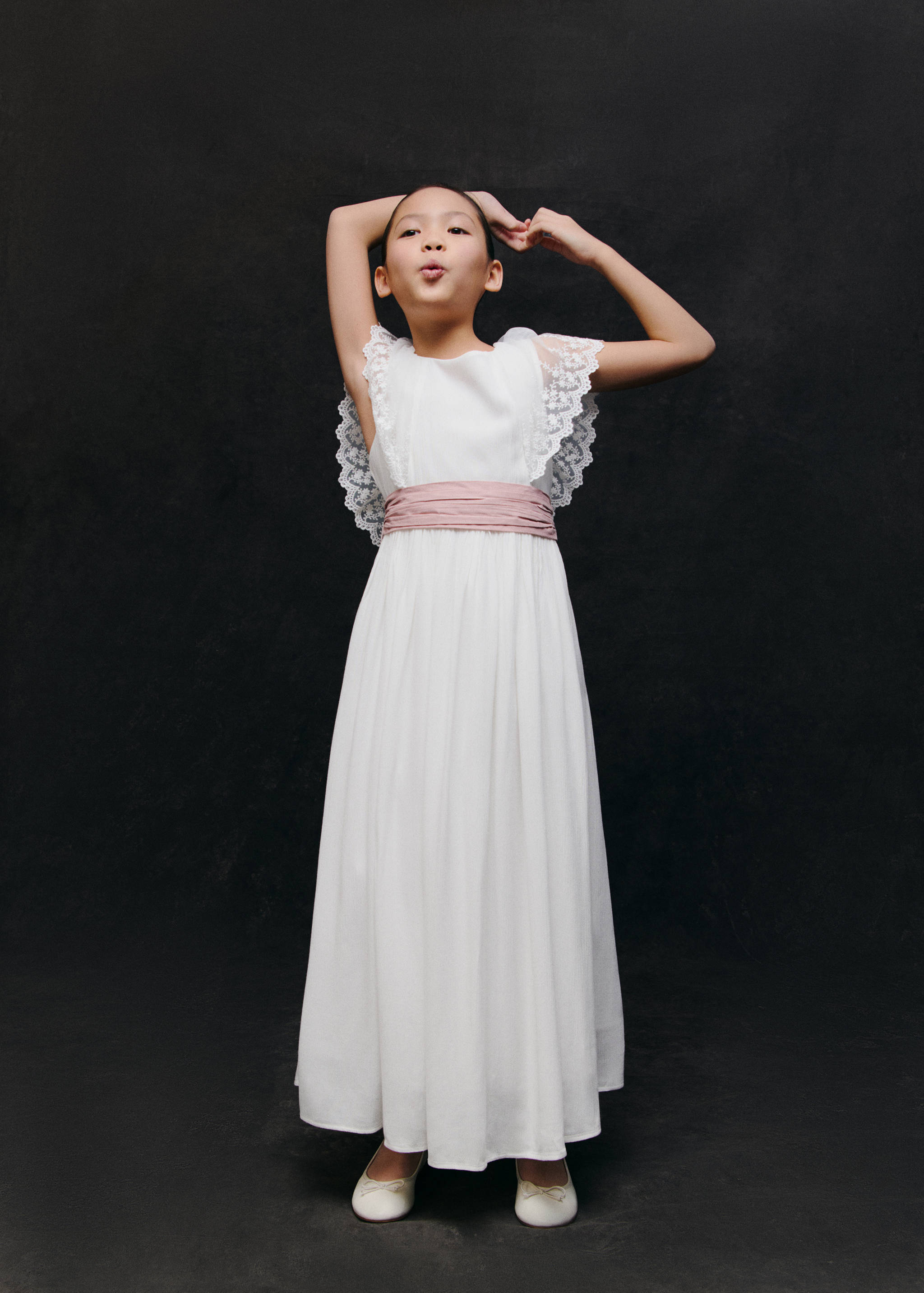 Long white dress with lace-trimmed shoulders and a pink sash.