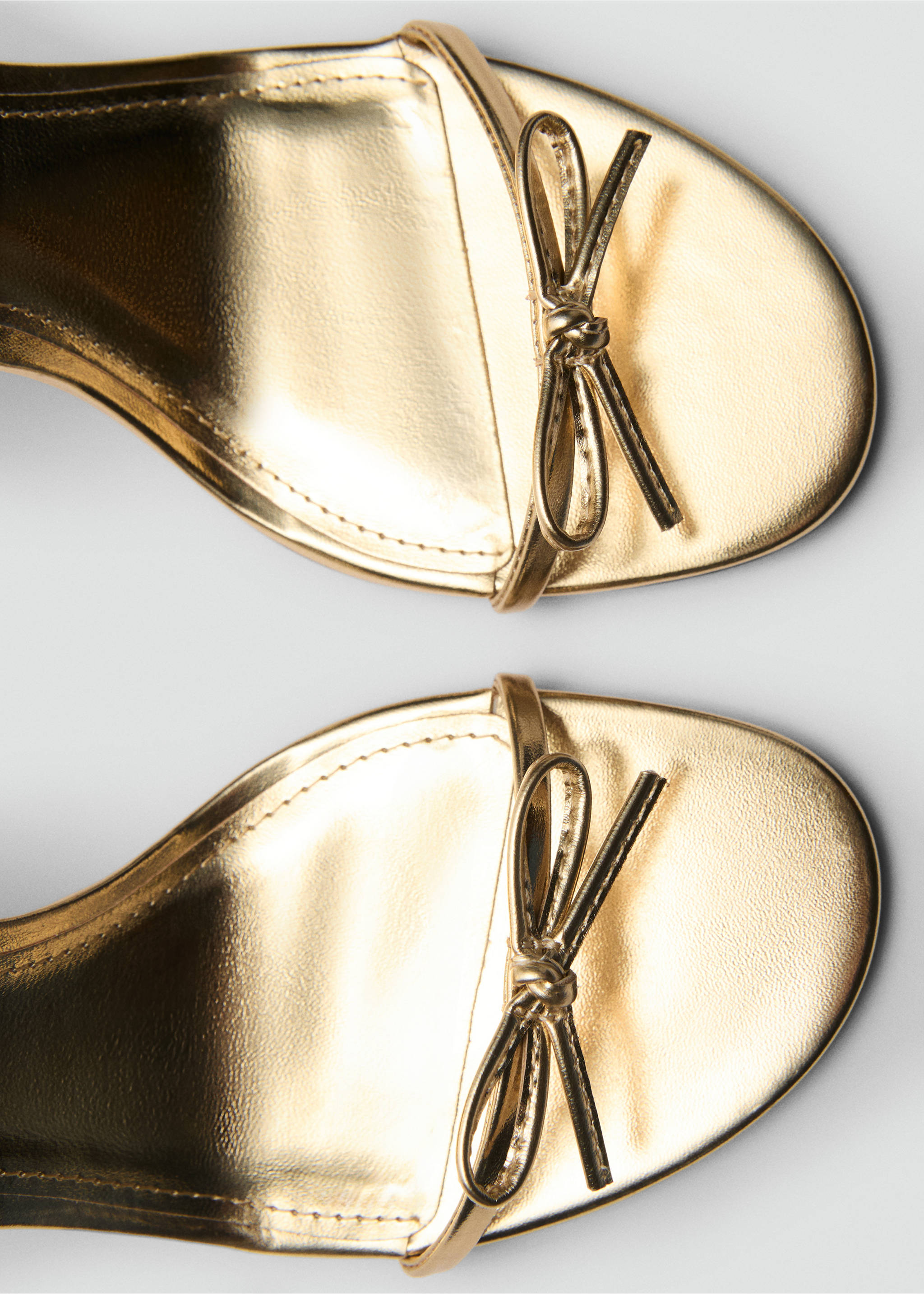 Close-up of gold metallic sandals with a front bow detail., Gold. Ref: 87064077-00.