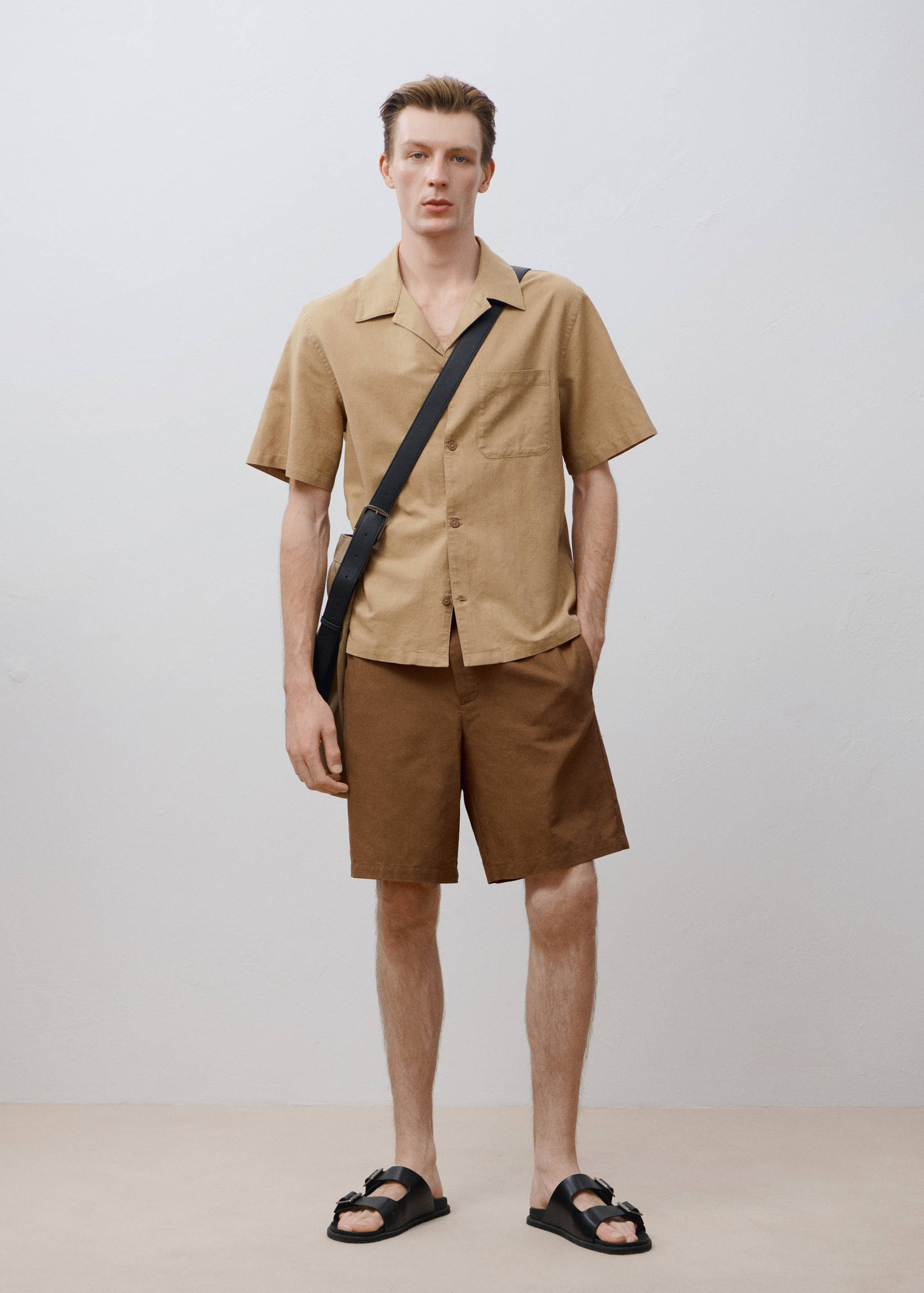 Bermudas marrones combinadas con una camisa beige de manga corta y sandalias negras.