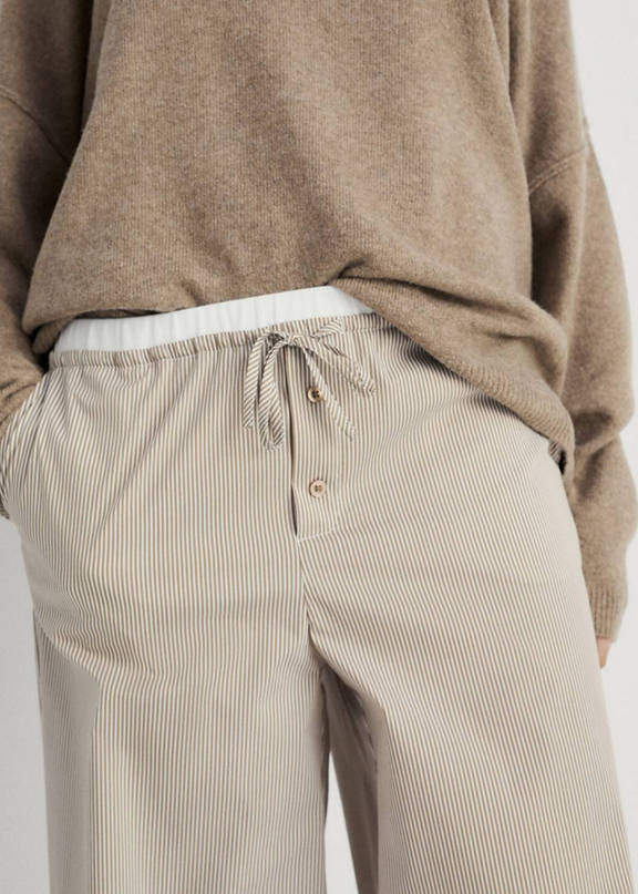Woman wearing a beige total look with wide trousers and jumper.