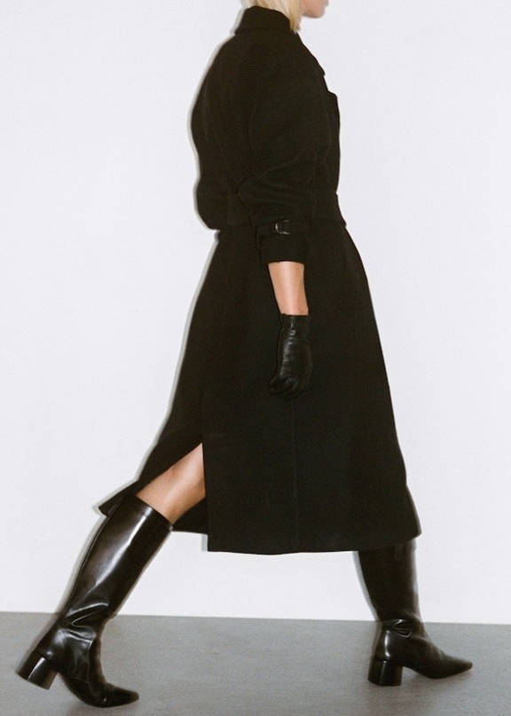 Woman wearing an outfit with black high boots, a long dress and a coat.