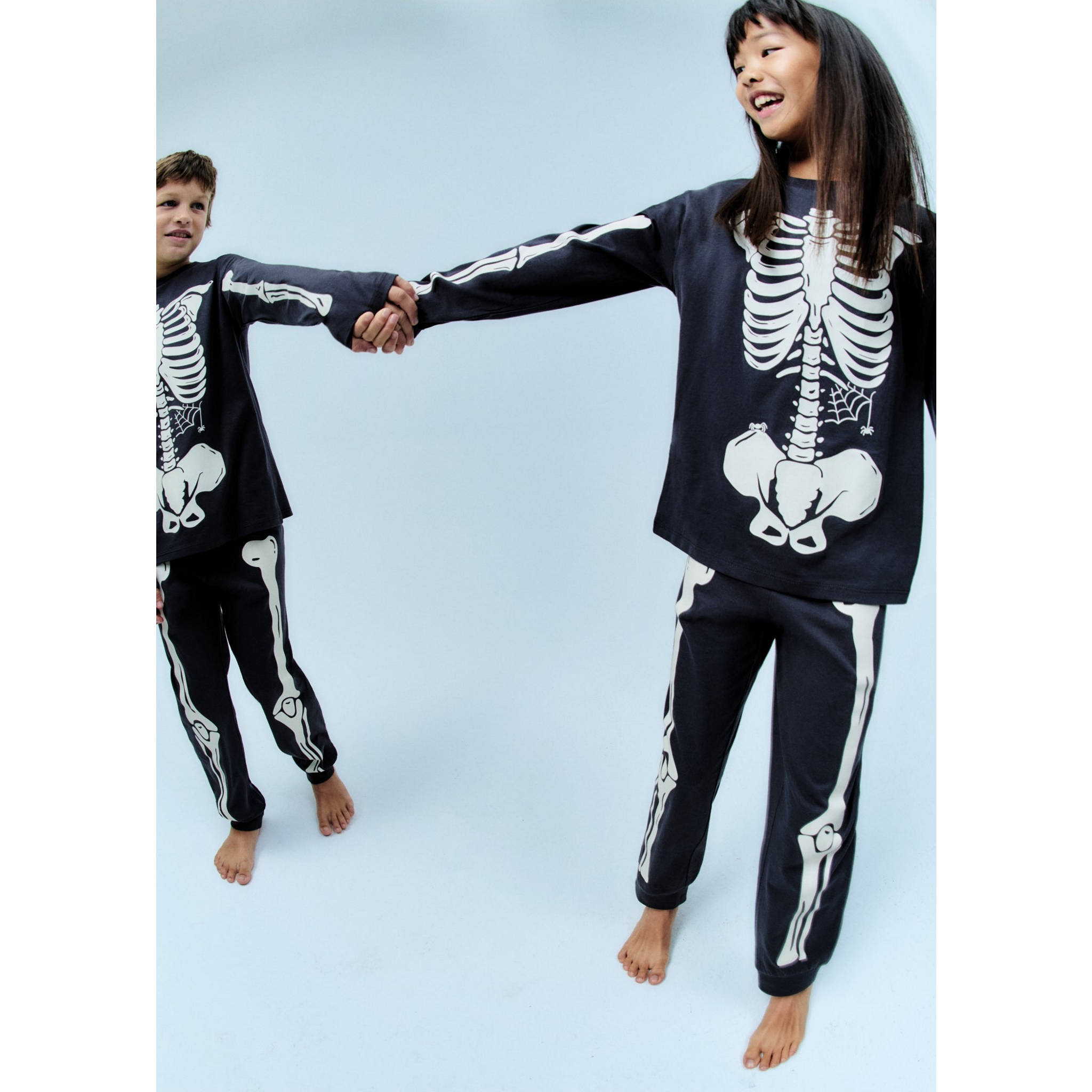 A boy and a girl dressed as skeletons playing with a Halloween pumpkin.