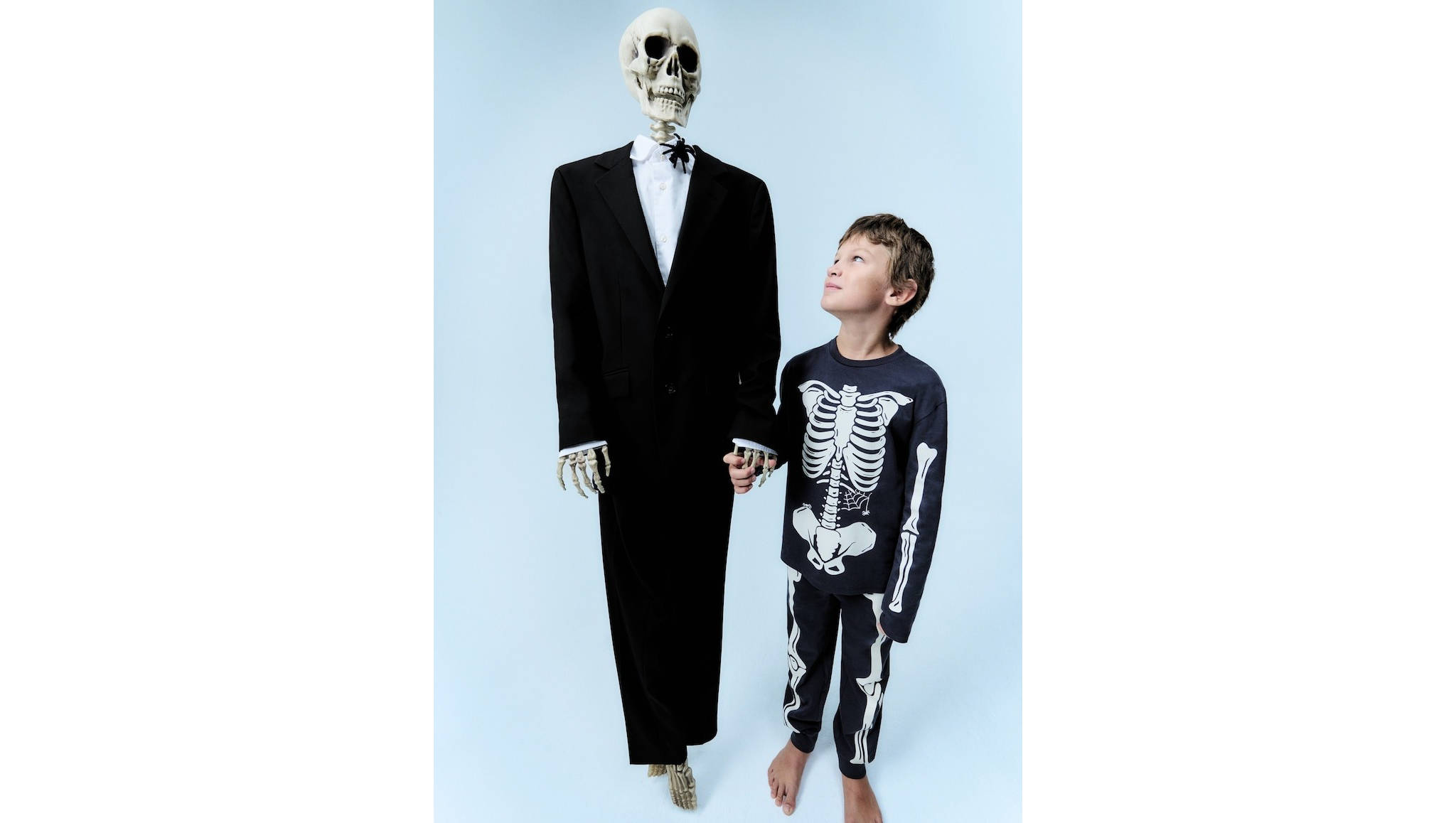 Niño disfrazado con un traje de esqueleto rodeado de calabazas de halloween