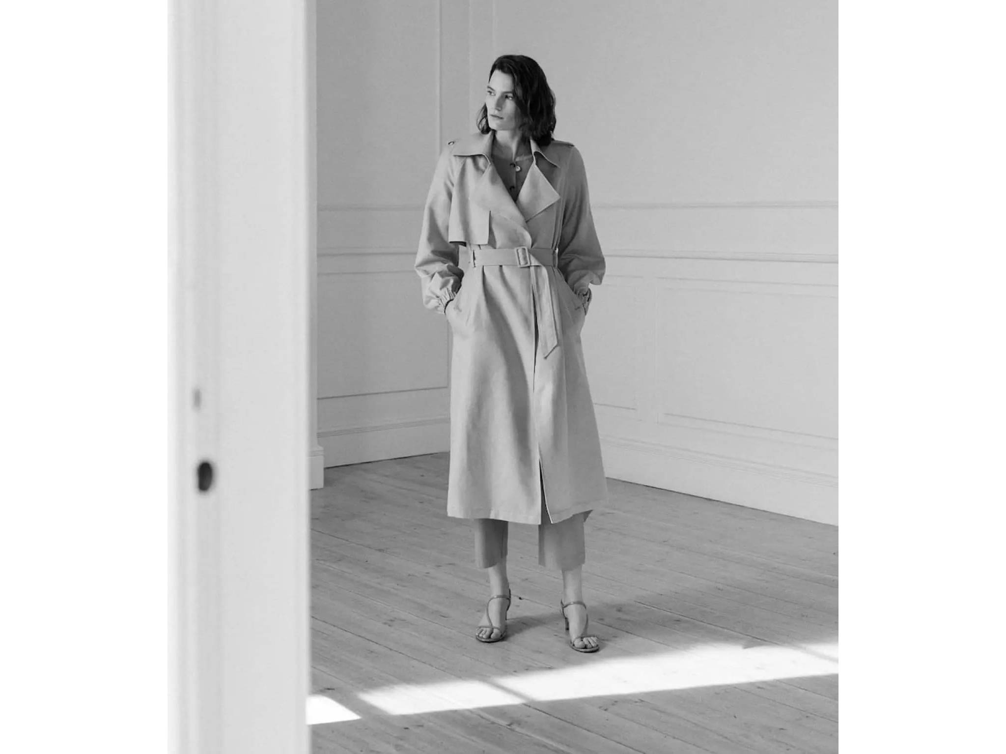 Black and white image of a woman wearing a long trench coat.