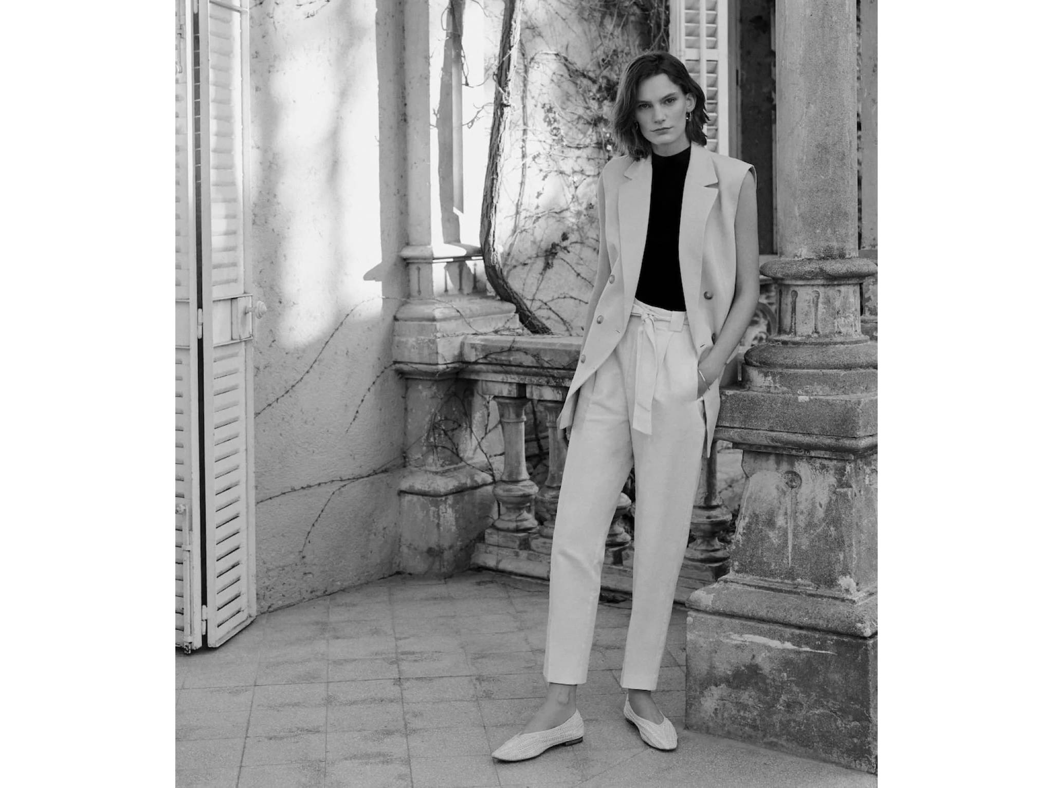 Black and white image of a woman wearing a sleeveless suit jacket.